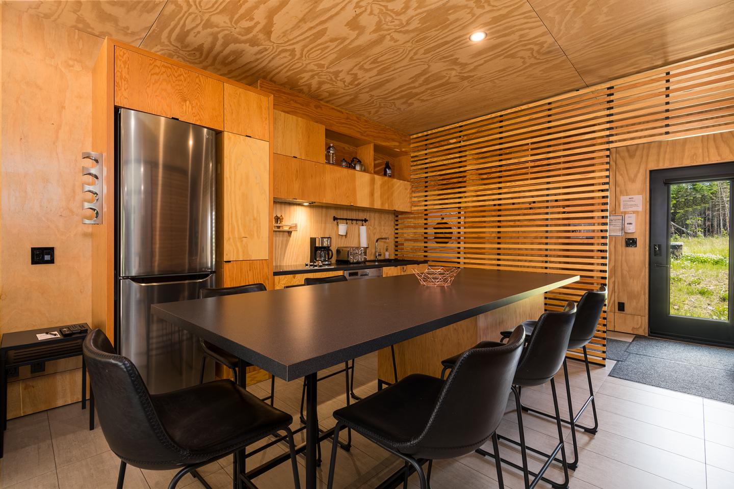 Cuisine moderne avec comptoir en bois, chaises noires et réfrigérateur en acier inoxydable.