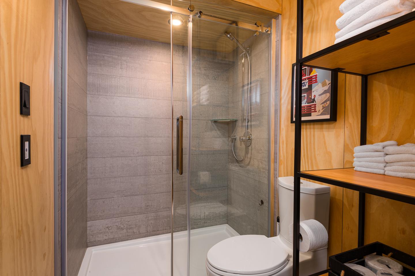 Salle de bain moderne avec douche, WC et étagères en bois.