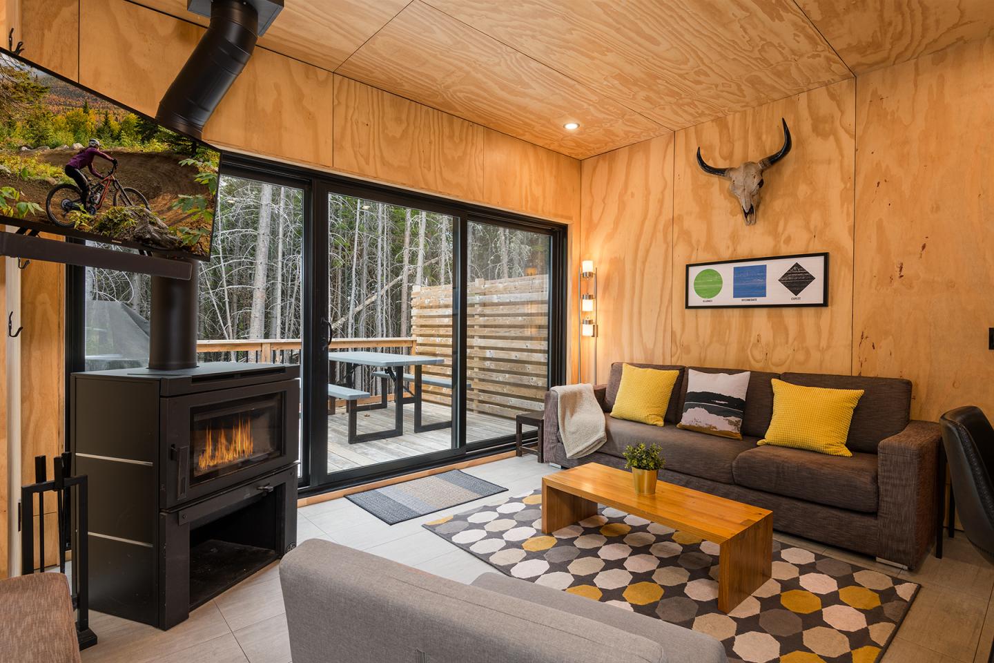 Salon moderne avec cheminée, canapé gris, coussins jaunes et table basse en bois.