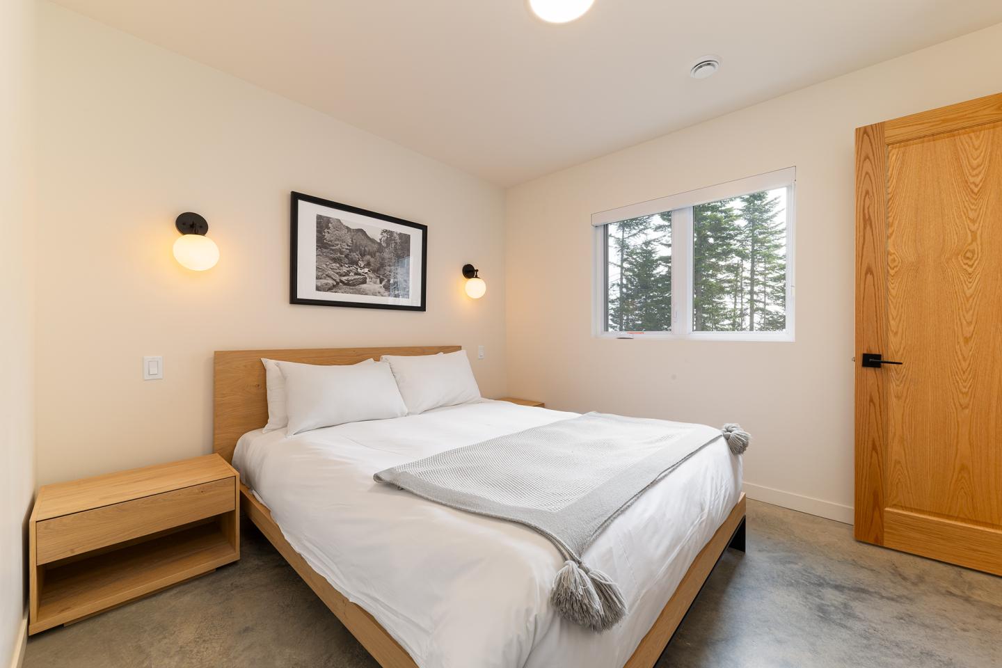 Chambre lumineuse avec lit double, table de chevet, et fenêtre donnant sur des arbres.