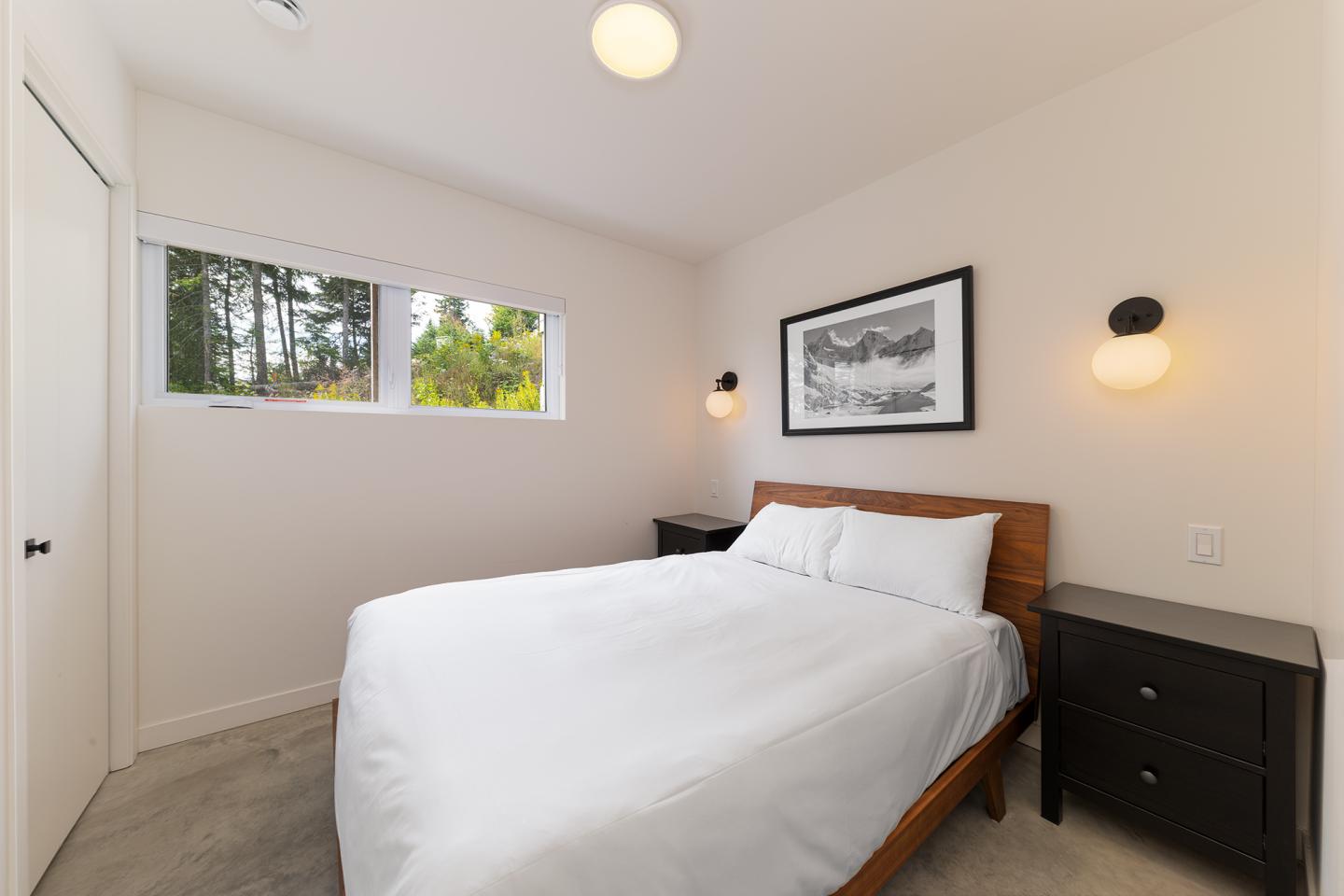 Chambre moderne avec lit double, murs blancs et grande fenêtre.