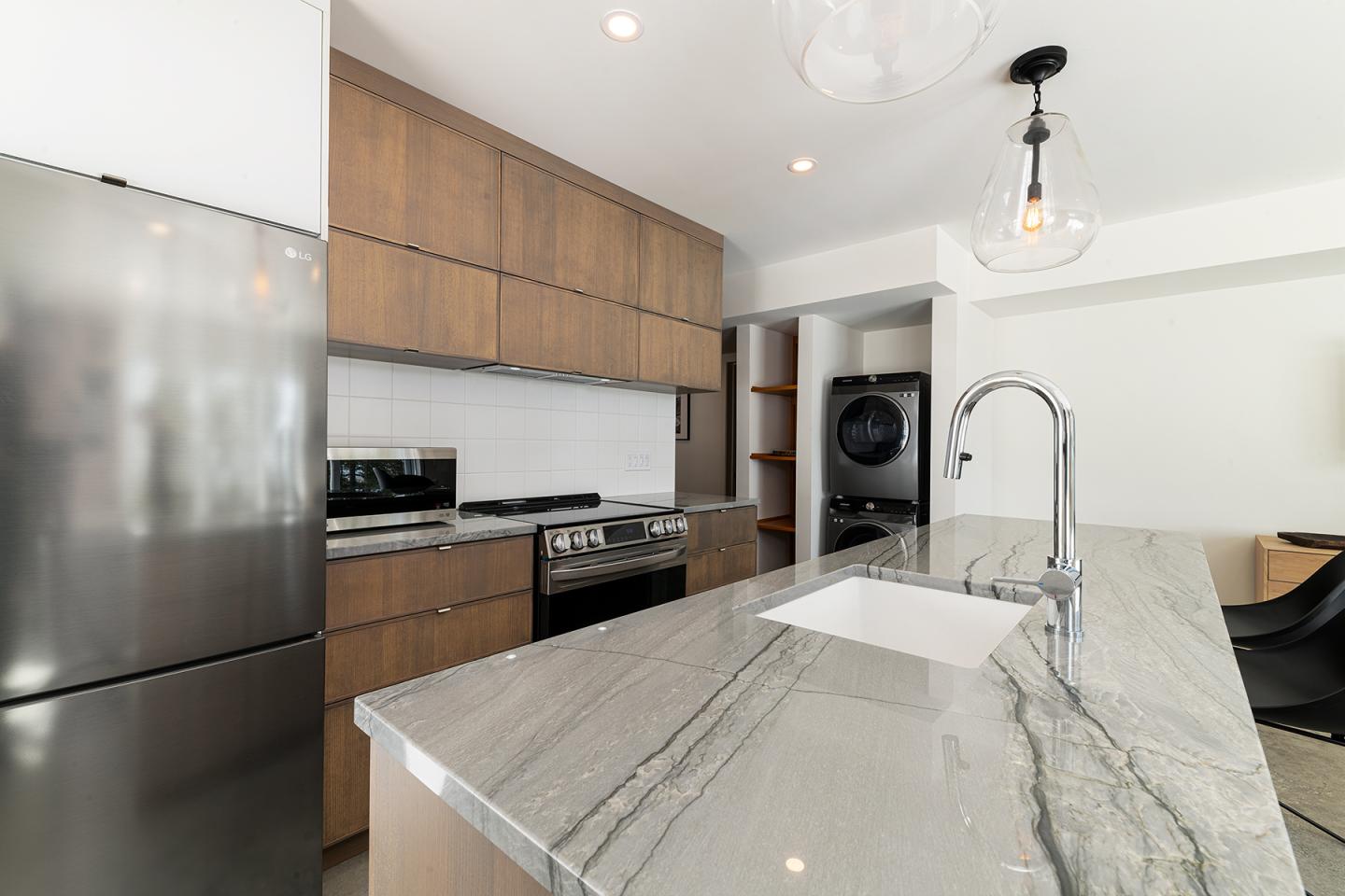 Cuisine moderne avec îlot en marbre, réfrigérateur en inox et luminaires suspendus.