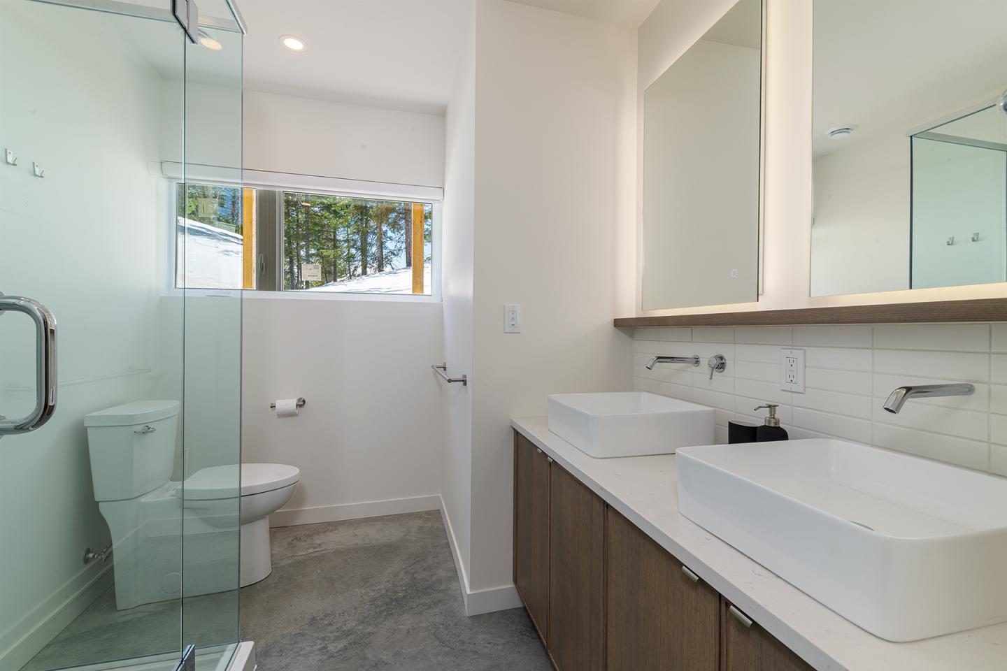 Salle de bain moderne avec deux lavabos, douche vitrée et toilettes blanches.