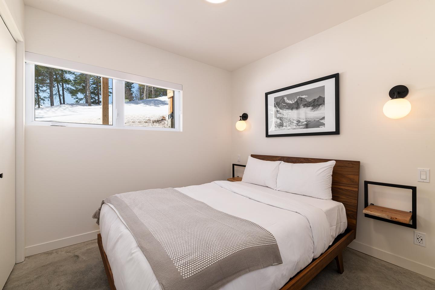 Chambre moderne avec un lit double, murs blancs, photo encadrée et fenêtres enneigées.