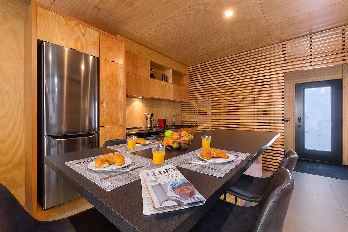 Cuisine moderne en bois, table avec croissants, jus d'orange et journal.