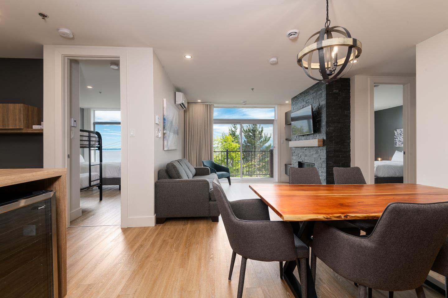 Intérieur moderne avec salon, table en bois, fenêtres ouvertes vers la nature.