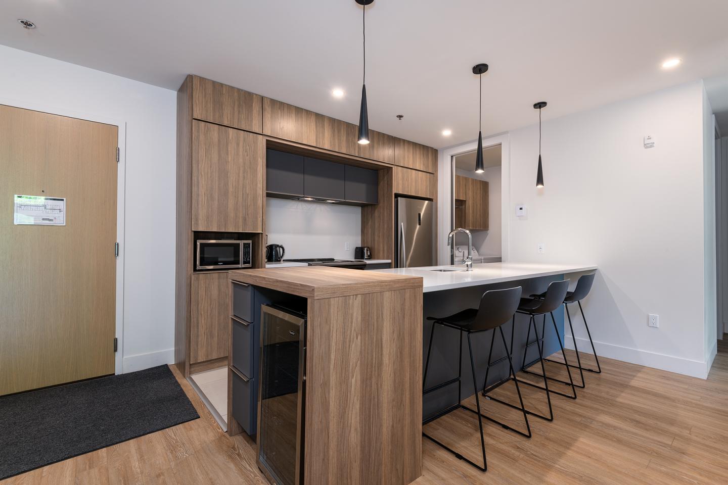 Cuisine moderne avec îlot central et tabourets noirs, éclairage suspendu.