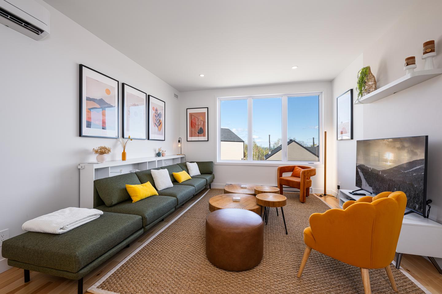 Salon moderne avec un canapé vert, fauteuil jaune, et grande fenêtre.