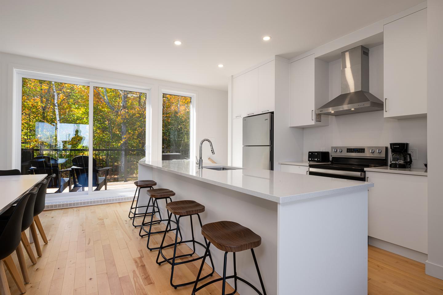 Cuisine moderne blanche avec îlot, tabourets et grande baie vitrée.