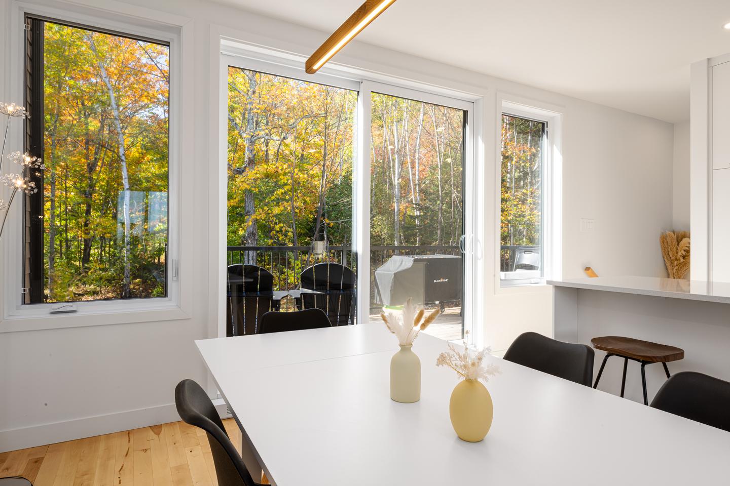 Salle à manger lumineuse avec vue sur des arbres d'automne par de grandes fenêtres.
