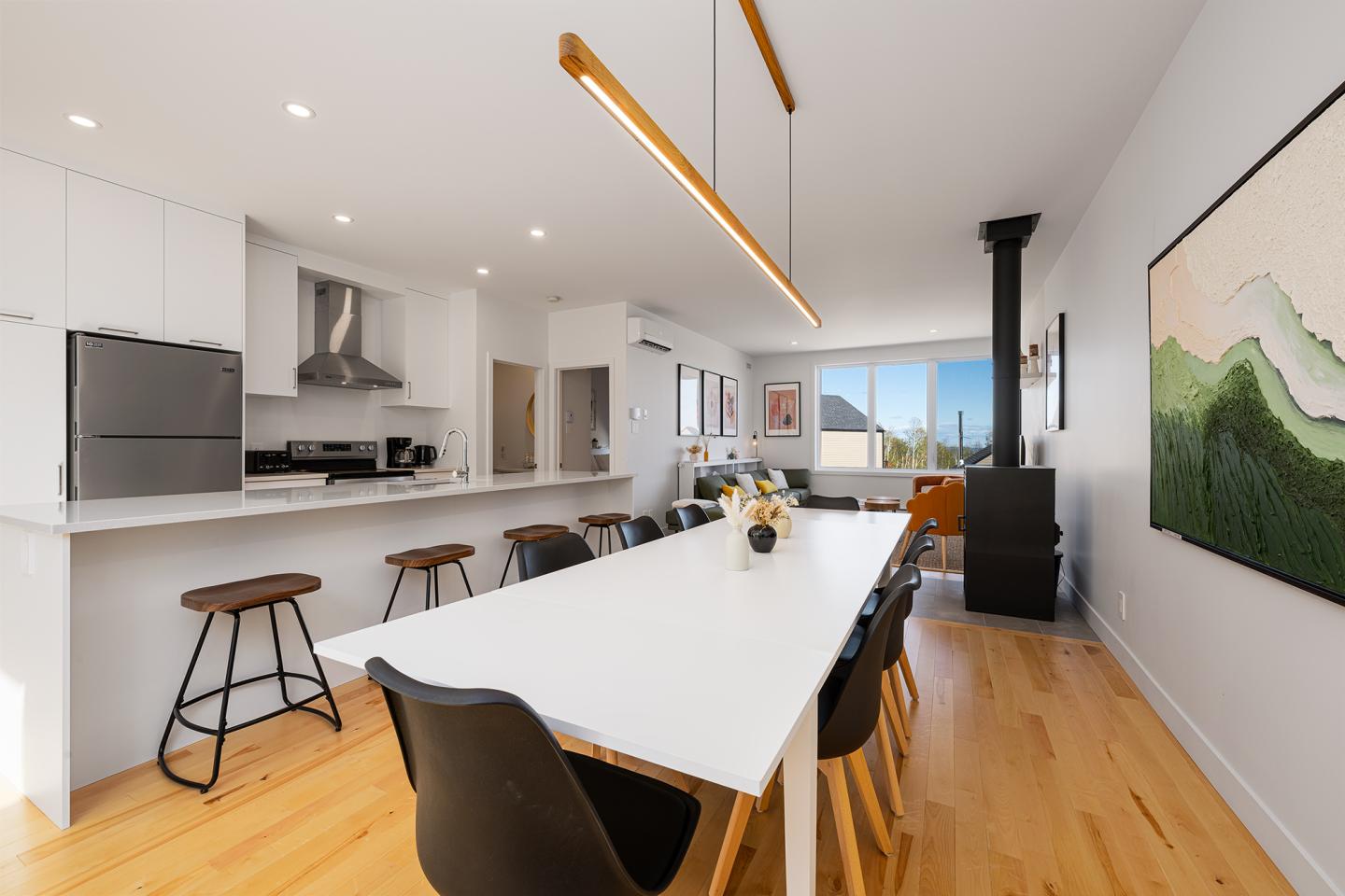 Cuisine moderne lumineuse avec table à manger, chaises noires, et grandes fenêtres.
