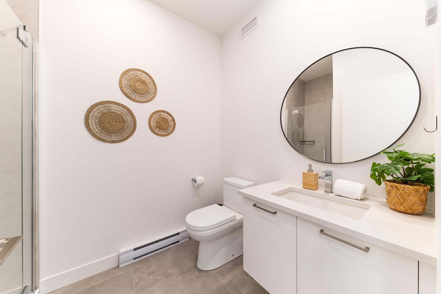 Salle de bain moderne blanche avec miroir ovale et décoration murale en osier.