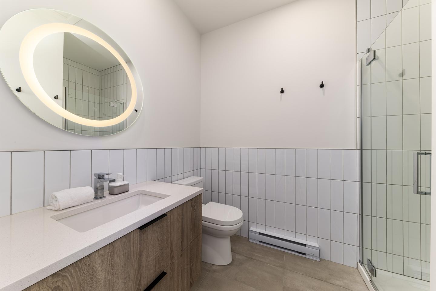 Salle de bain moderne avec miroir ovale, lavabo, douche vitrée et murs blancs.