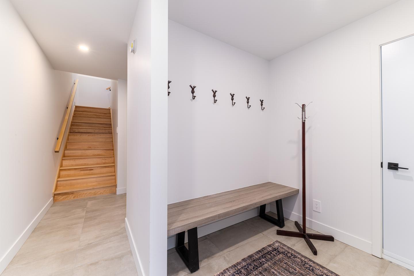 Vestiaire avec banc en bois, crochets au mur, et escalier en bois.