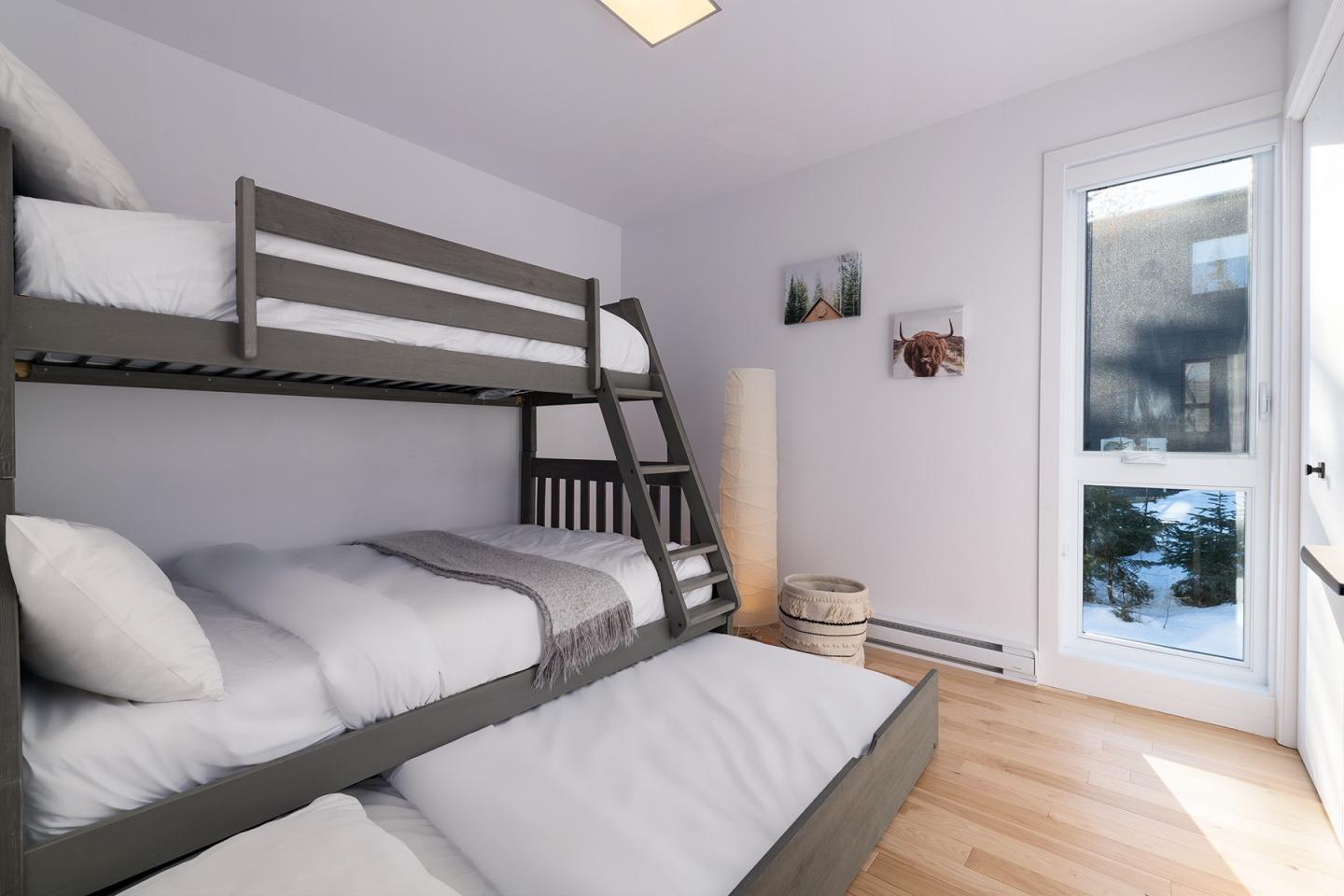 Chambre lumineuse avec lits superposés, parquet, et grande fenêtre.