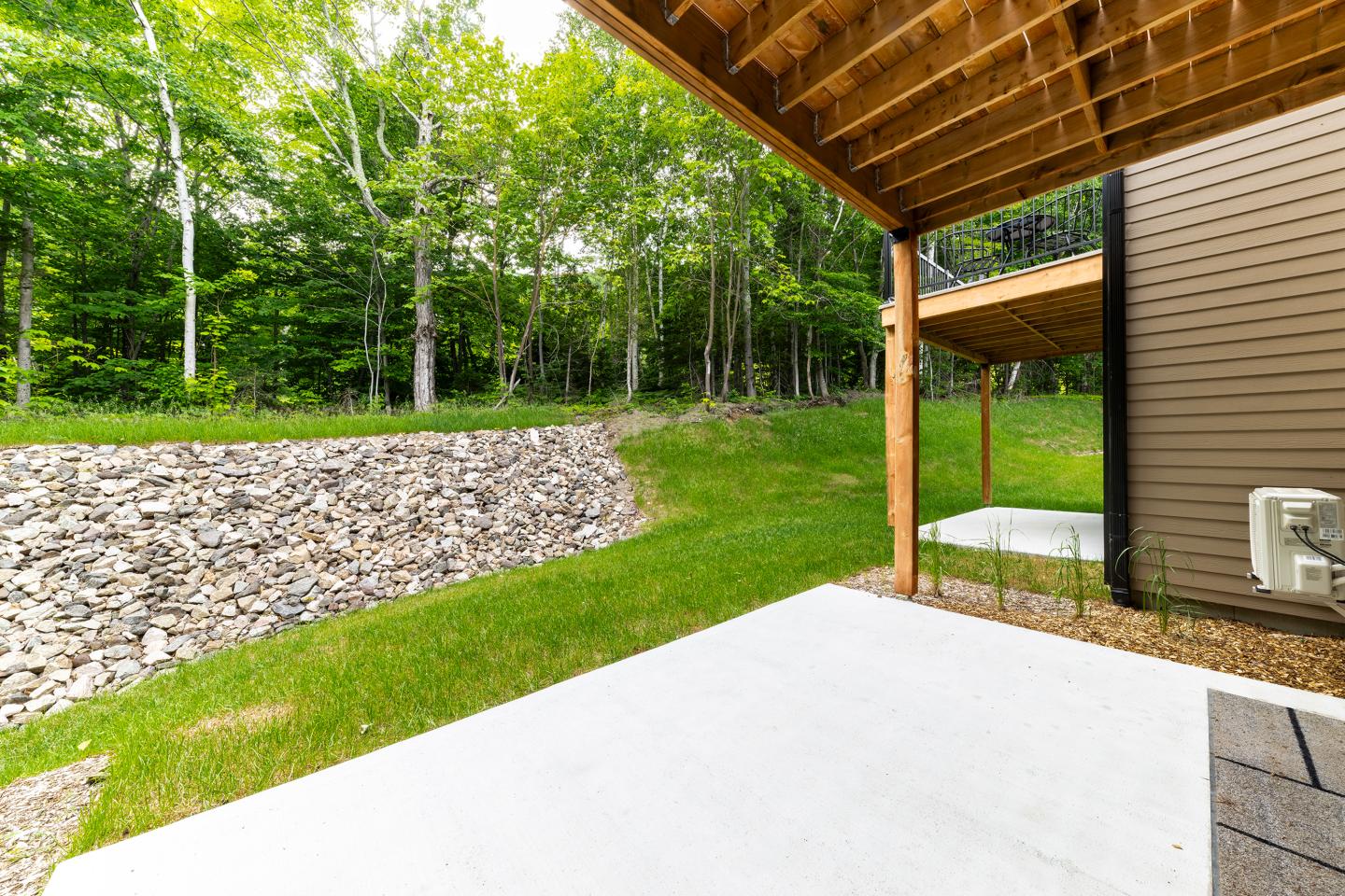 Terrasse en béton avec toit en bois, vue sur pelouse et arbres.