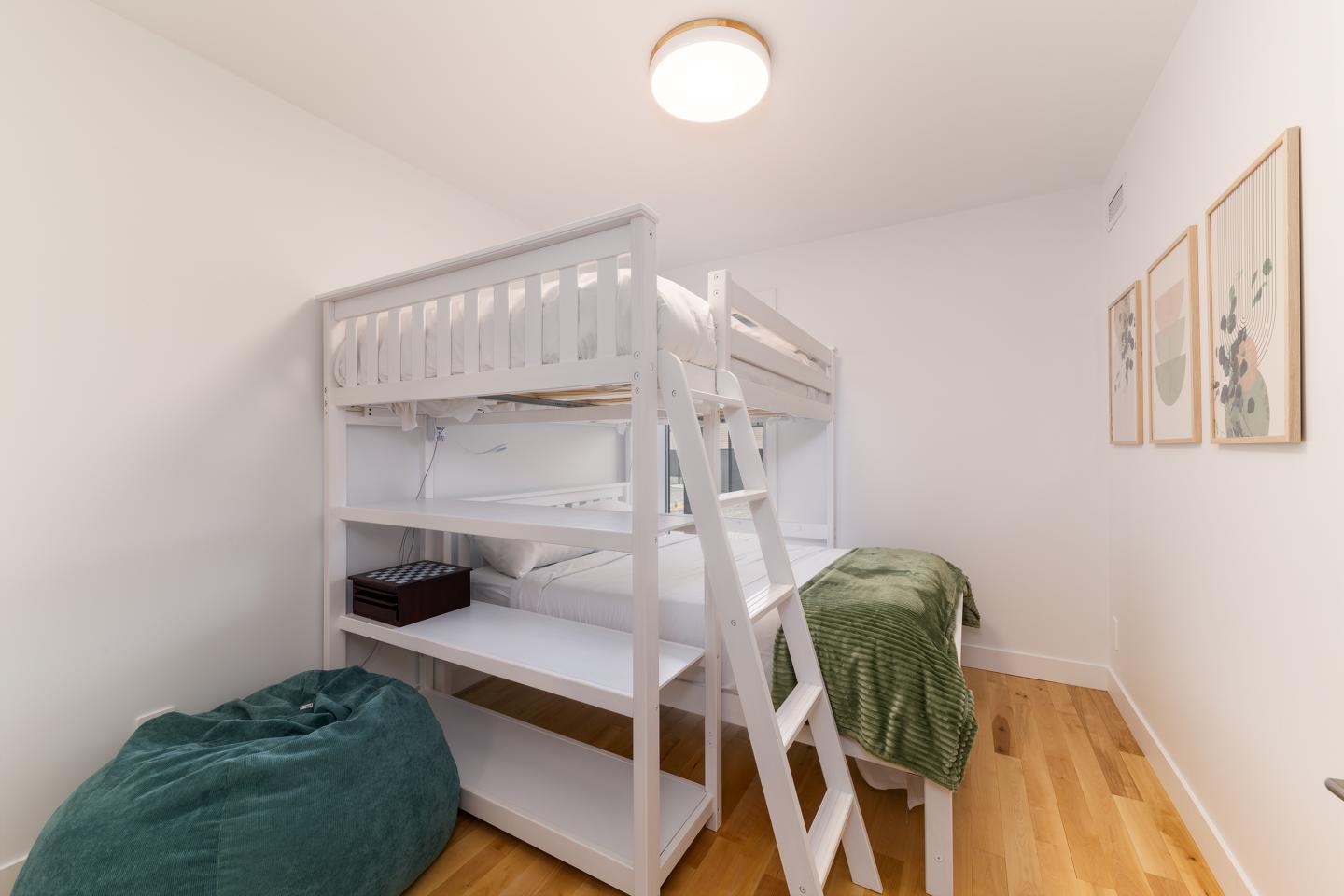 Lit superposé blanc avec couverture verte, coussin et parquet clair.
