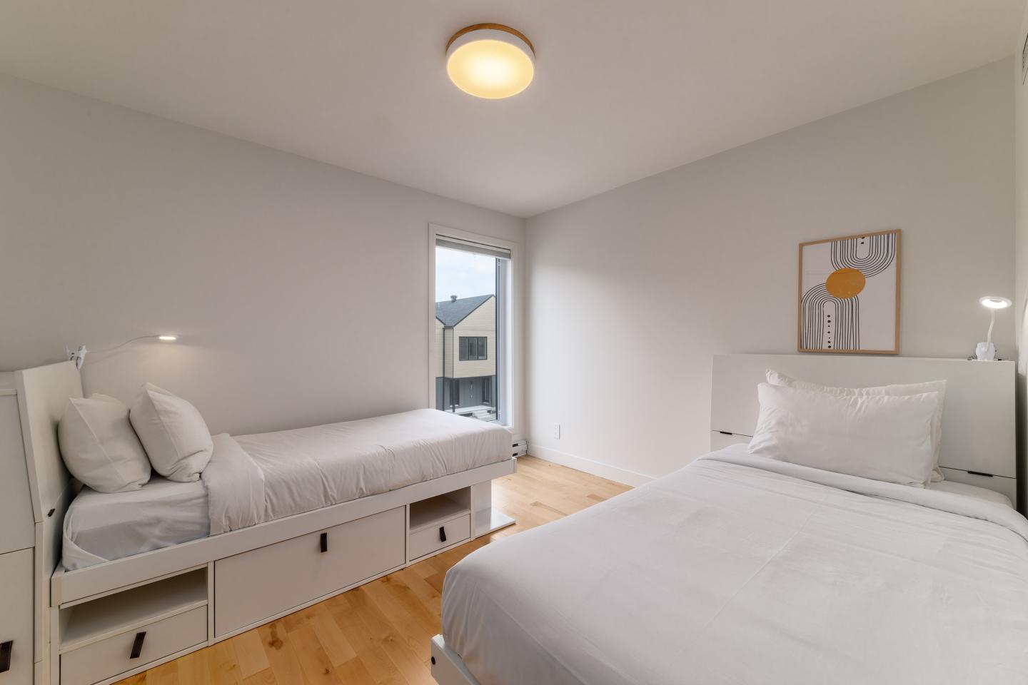 Deux lits blancs dans une chambre lumineuse avec parquet en bois clair.