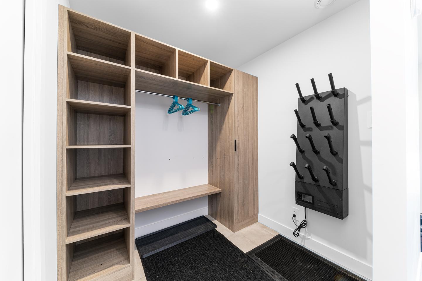 Vestiaire moderne avec étagères en bois et supports à chaussures noirs.