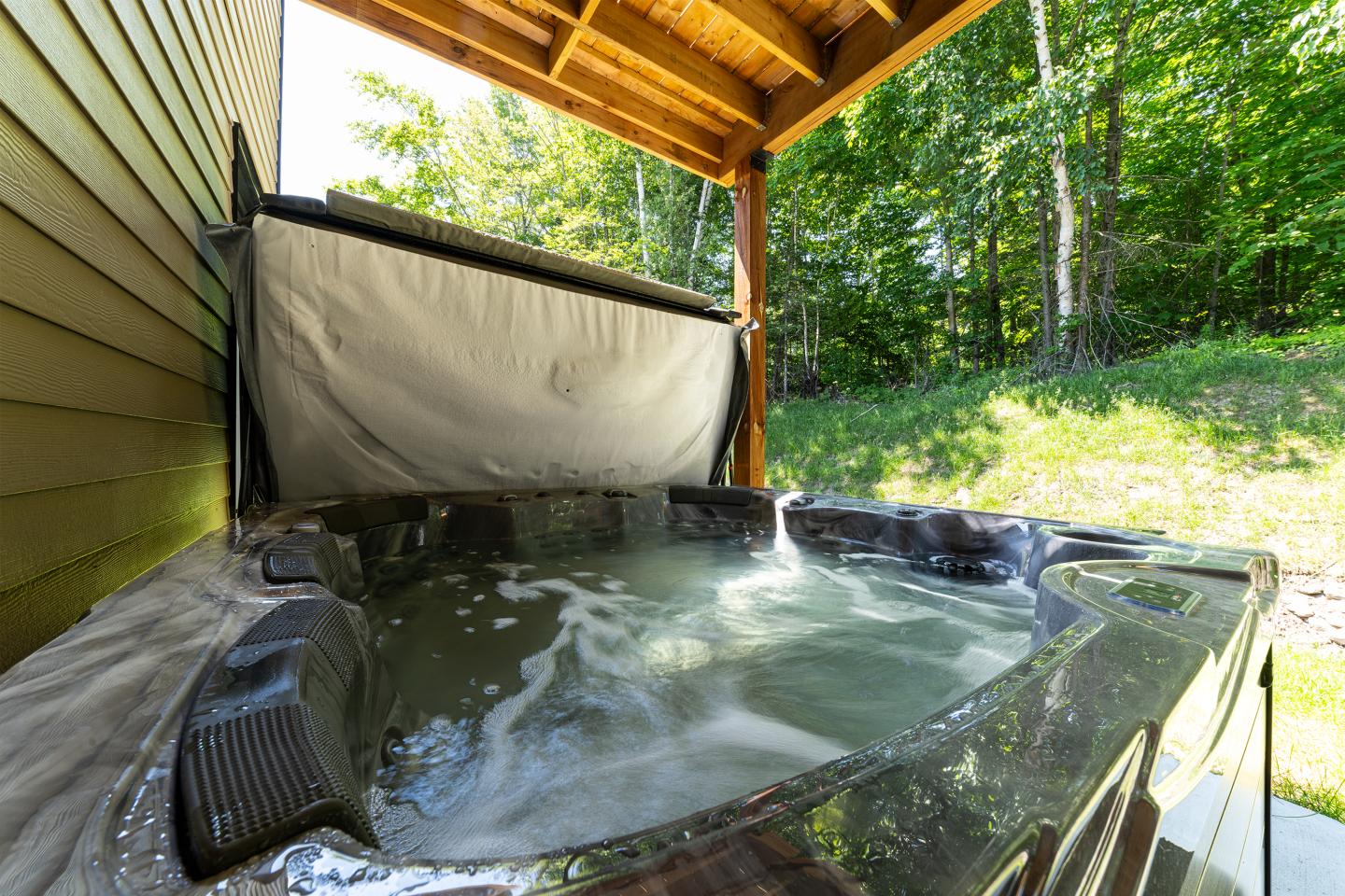 Spa extérieur sous auvent, eau bouillonnante, forêt en arrière-plan.