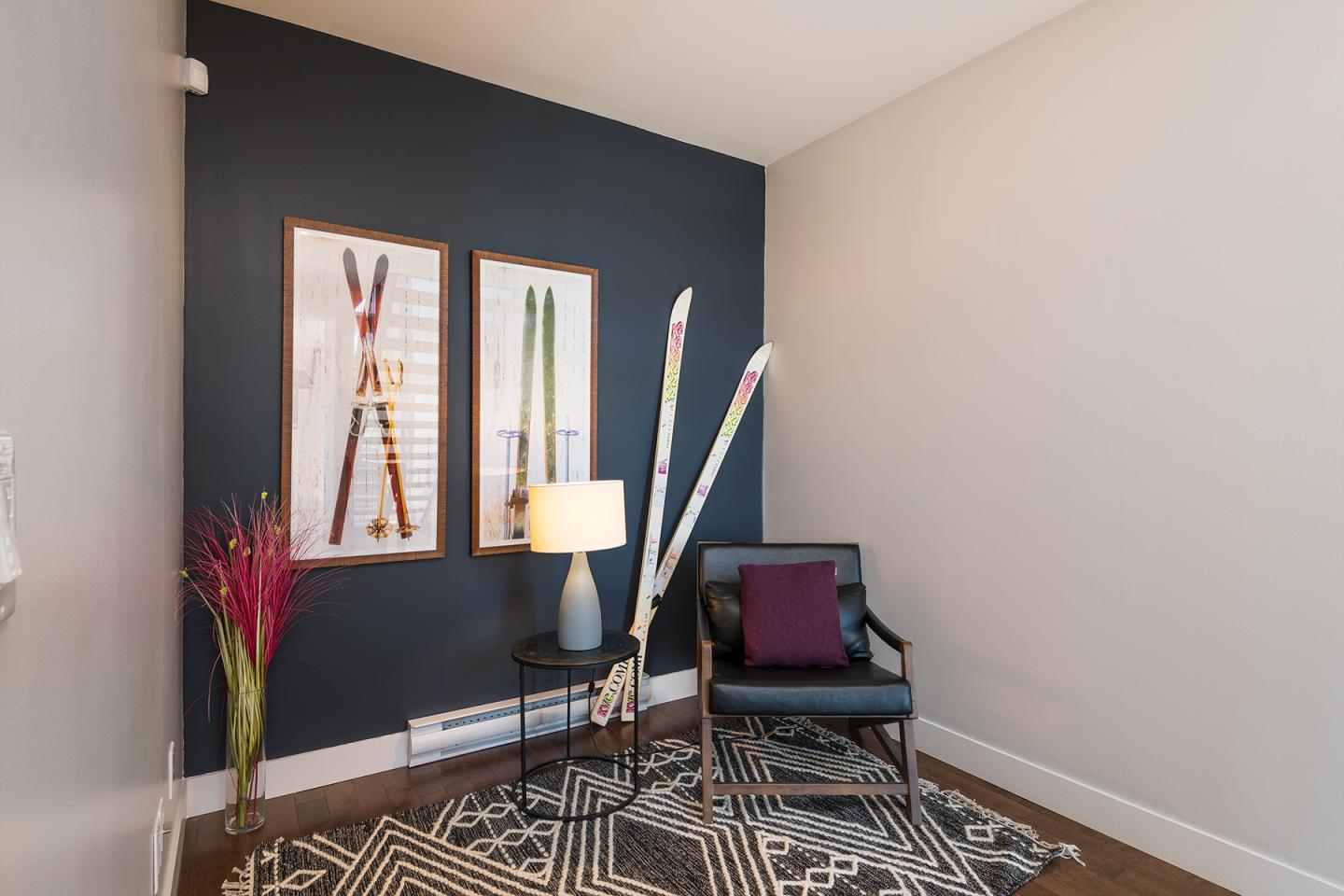 Coin salon moderne avec fauteuil, ski décoratif, tapis géométrique et lampe sur table.