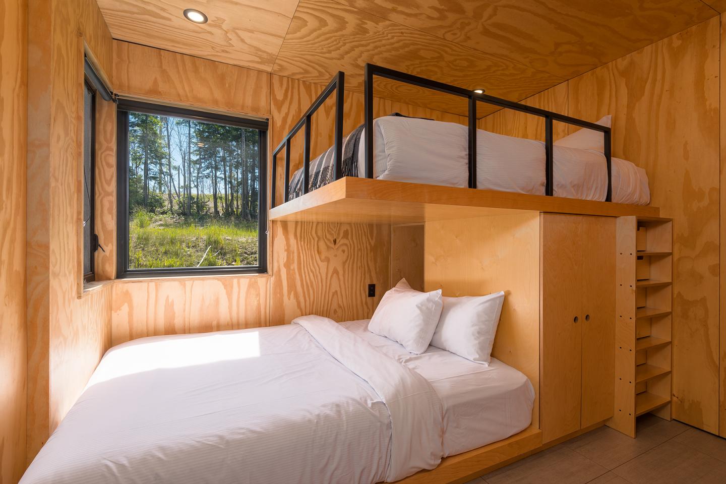Chambre en bois avec lit superposé, fenêtre sur forêt.