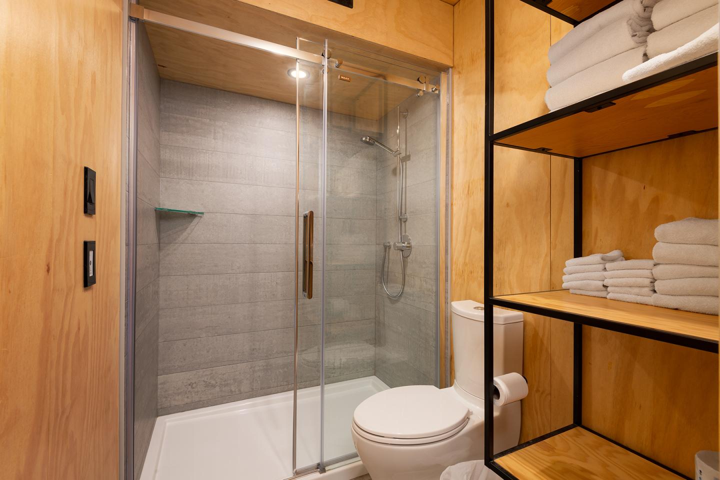 Salle de bain moderne avec douche vitrée et étagères en bois avec serviettes pliées.