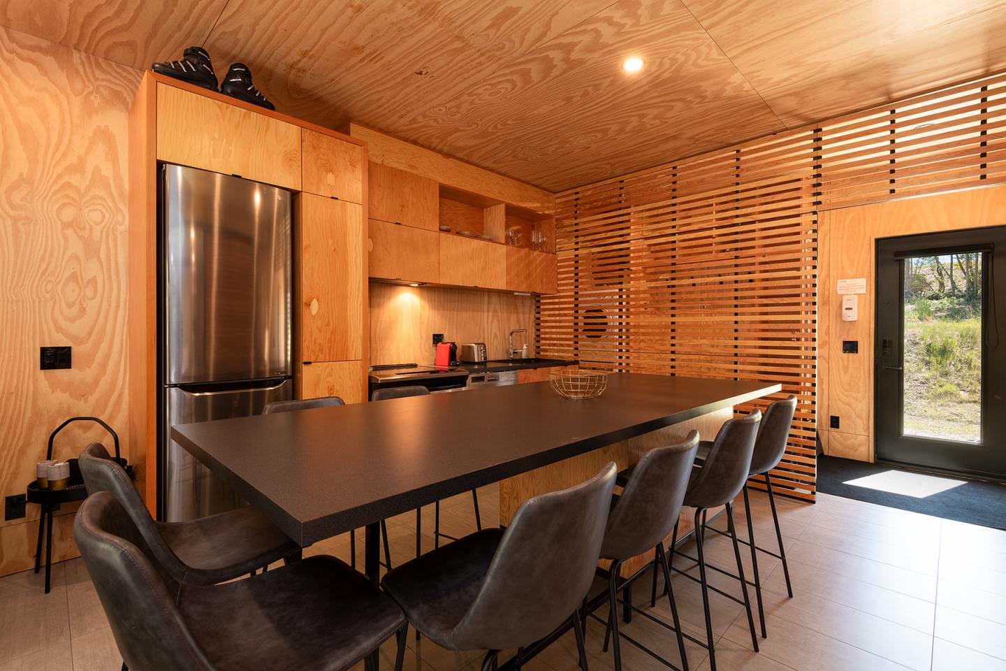 Cuisine moderne avec table noire, chaises sombres et réfrigérateur en acier inoxydable.