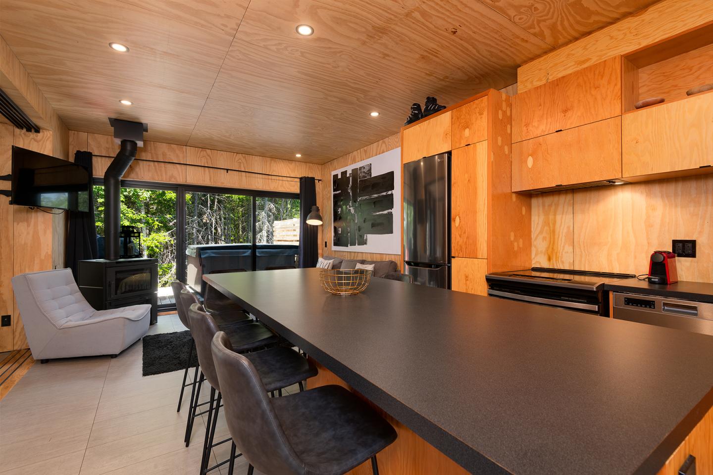 Cuisine moderne en bois clair avec îlot central, grandes fenêtres et coin salon.