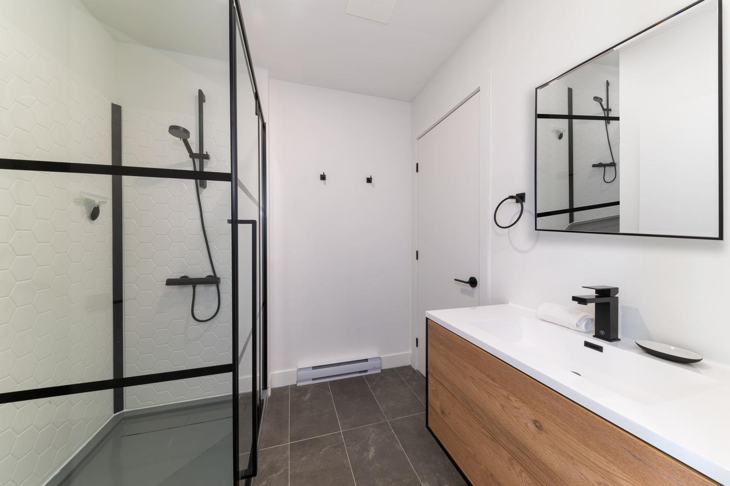 Salle de bain moderne avec douche vitrée, lavabo en bois et miroir.