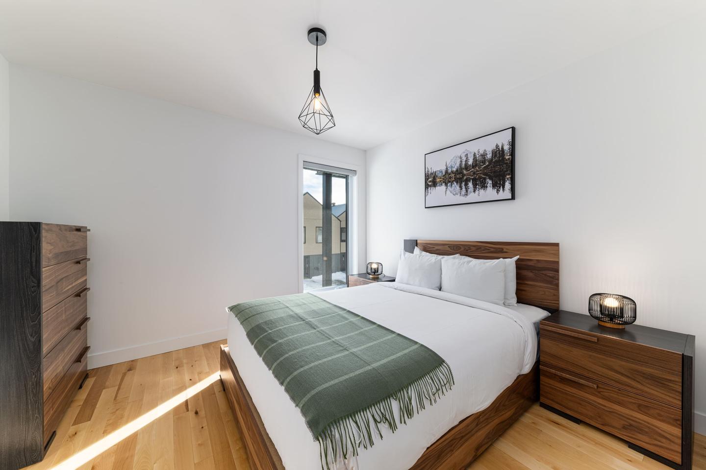 Chambre moderne, lit double avec couverture verte, meubles en bois, fenêtre.