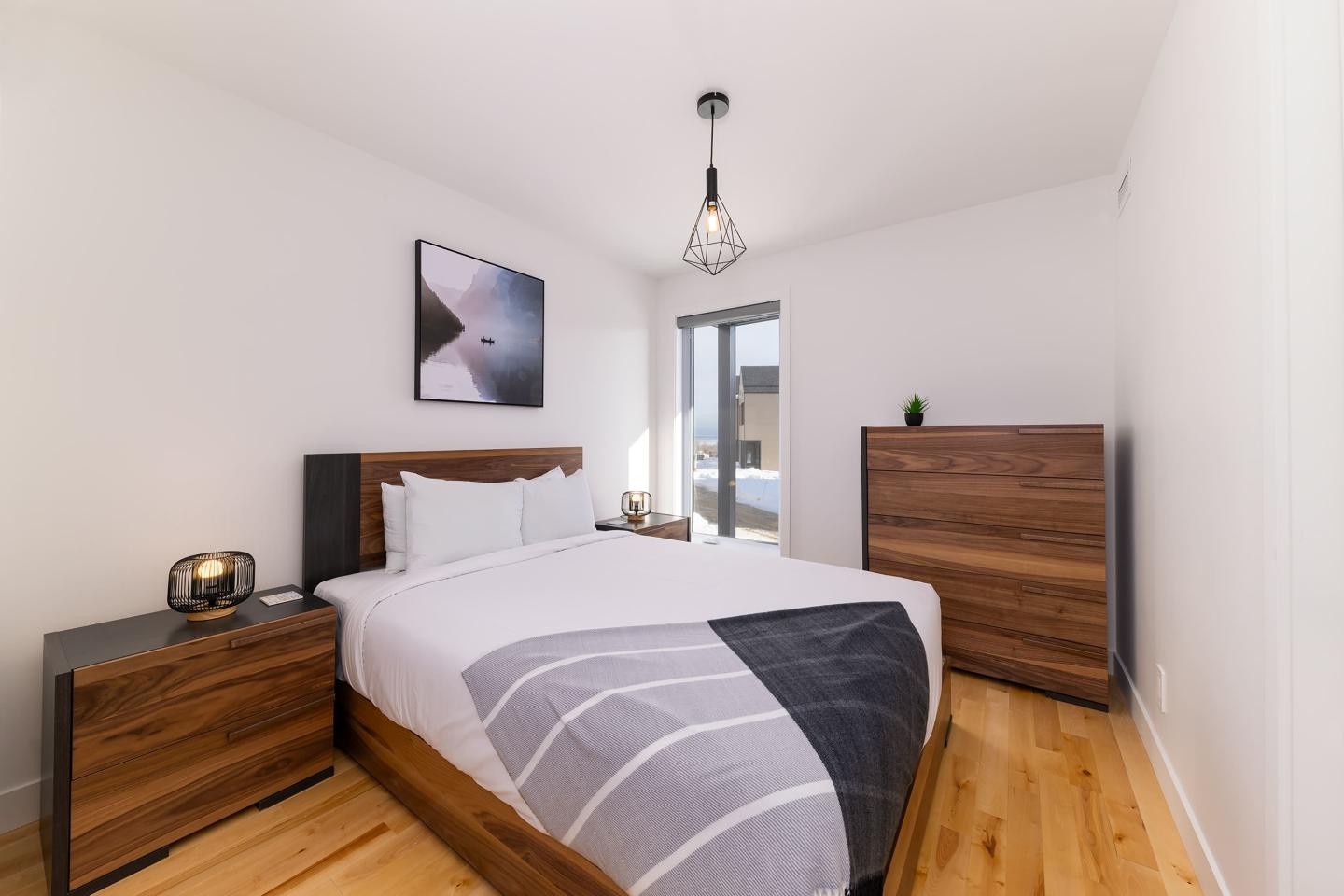 Chambre moderne avec lit double, commodes en bois et tableau au mur.
