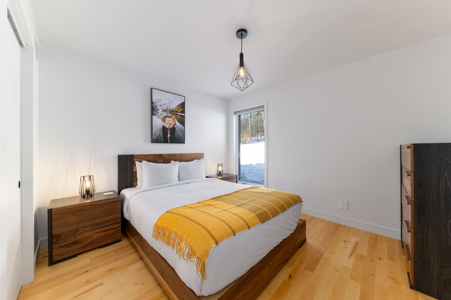 Chambre moderne avec lit double, couvre-lit jaune, lampes stylées et parquet en bois clair.