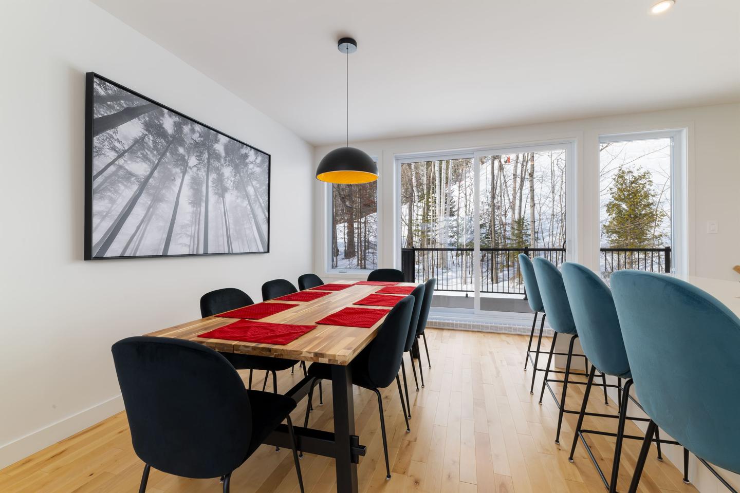 Salle à manger moderne avec table en bois, chaises noires et vue sur la neige.