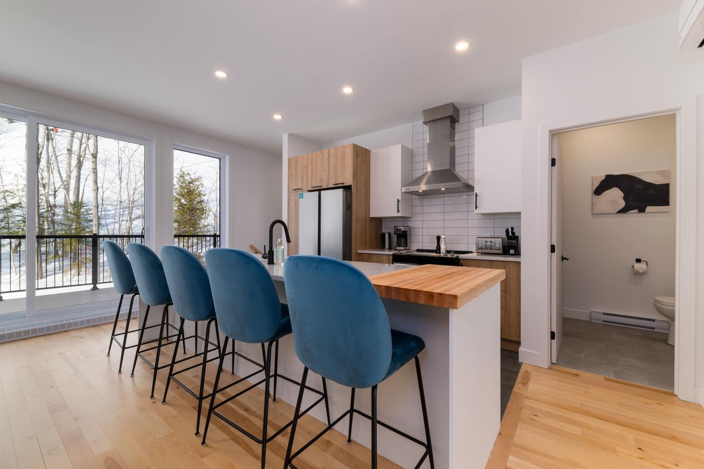 Cuisine moderne avec tabourets bleus et accès à une terrasse ensoleillée.