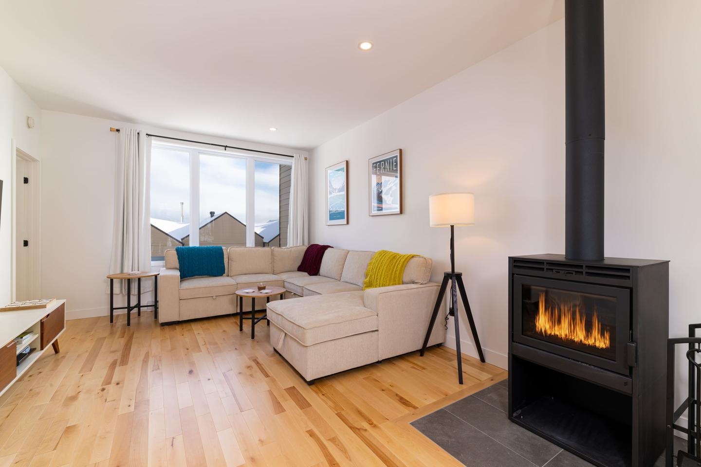 Salon moderne avec canapé d'angle, poêle à bois et parquet clair.