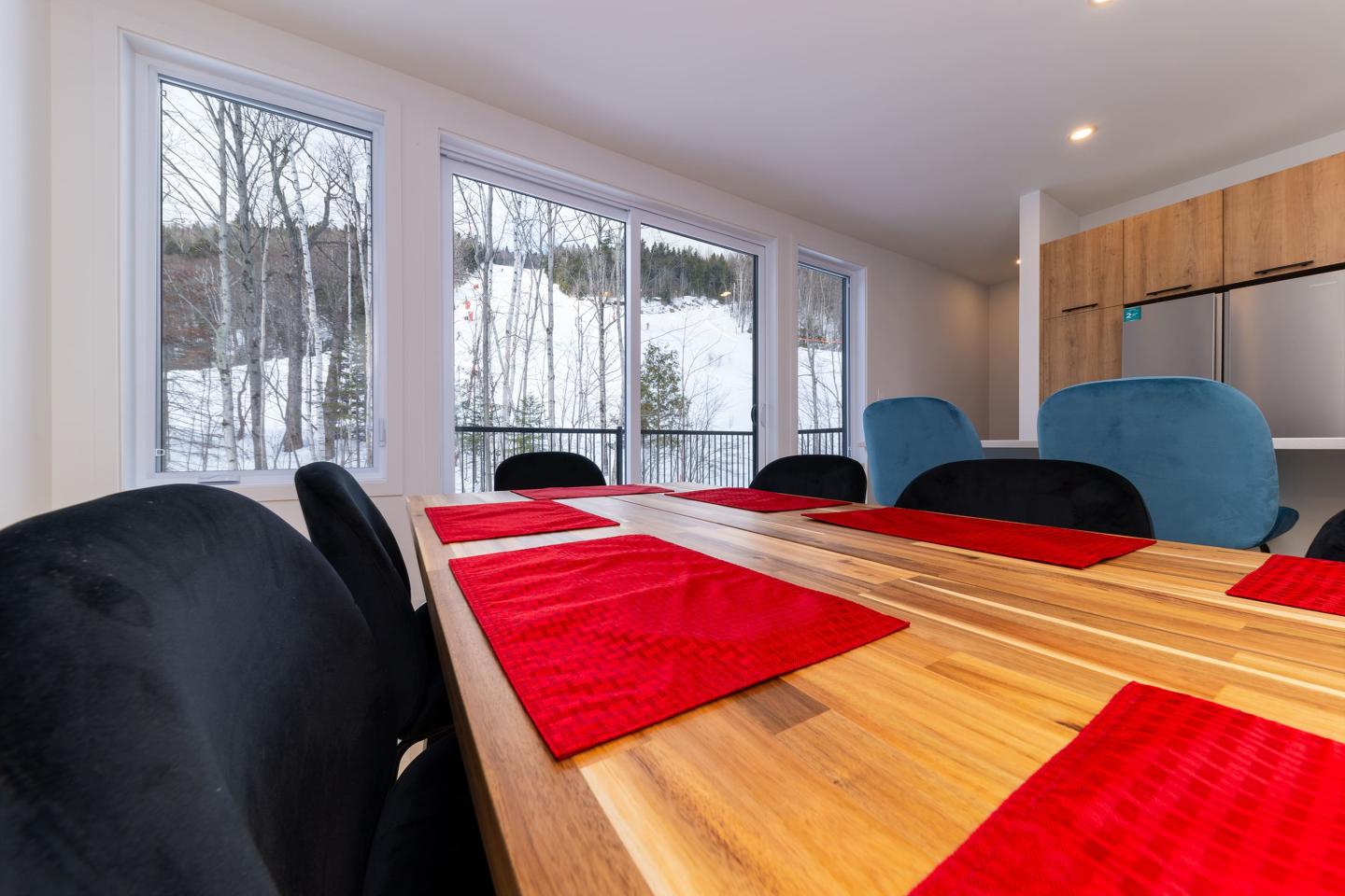 Table en bois avec sets de table rouges, vue sur l'extérieur enneigé par des fenêtres.
