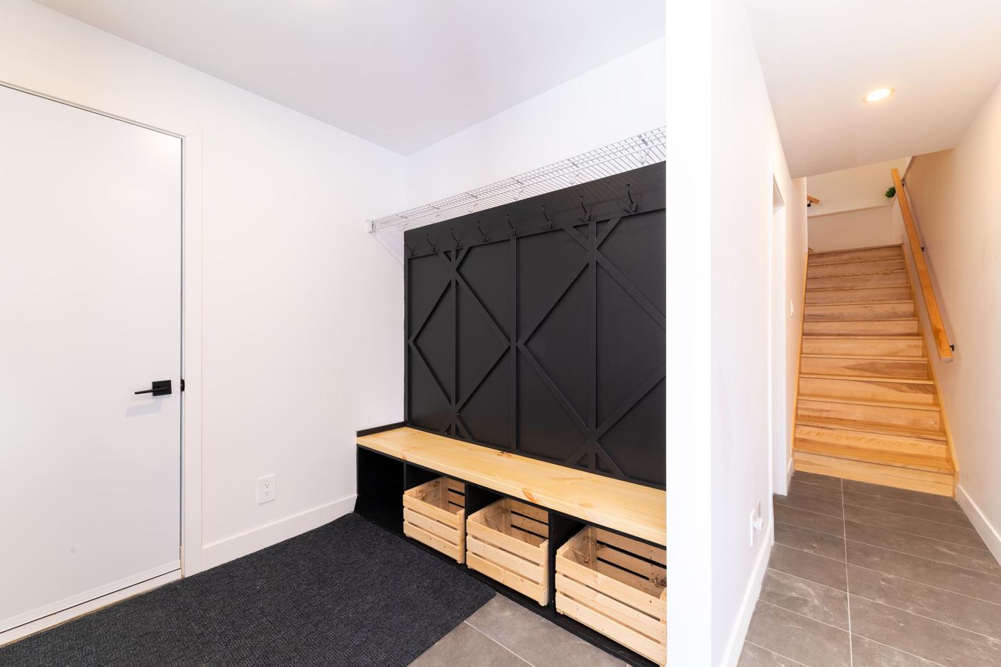 Couloir avec escalier, banc de rangement et porte blanche.