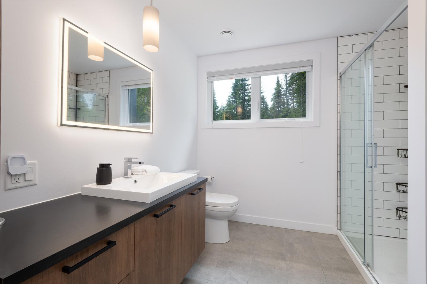 Salle de bain moderne avec douche vitrée, lavabo et miroir lumineux.