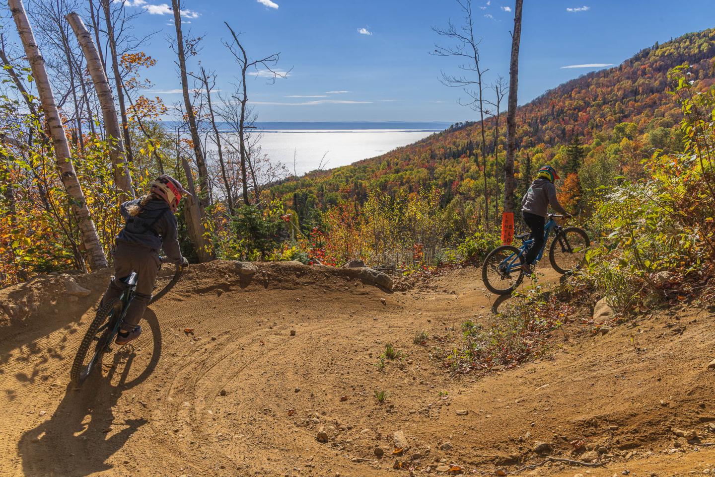 Deux cyclistes en VTT sur un sentier de montagne en automne, vue sur un lac.