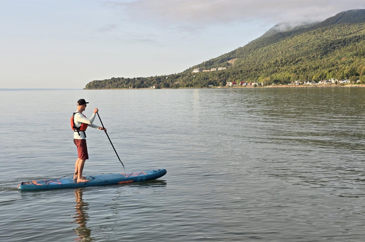 Homme sur une planche à pagaie sur un lac calme, montagne en arrière-plan.