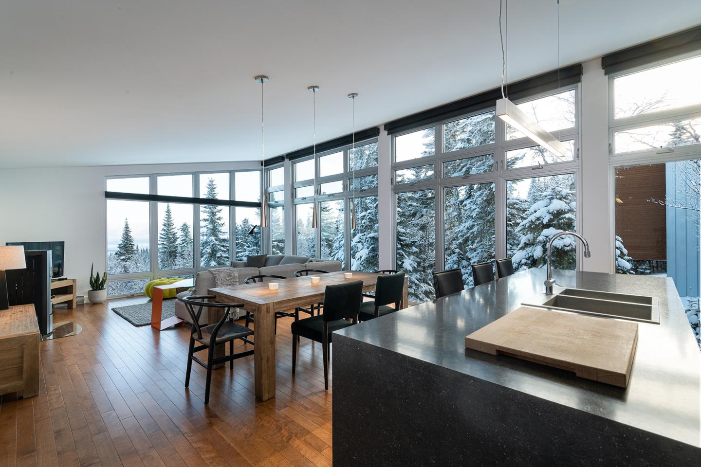 Salle à manger moderne avec baies vitrées, vue sur forêt enneigée.