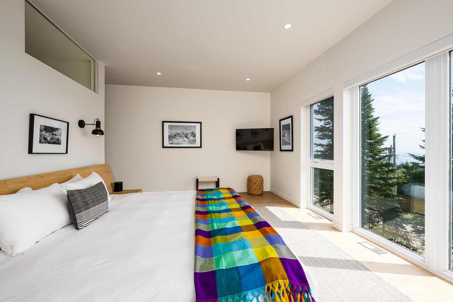 Chambre moderne, lit avec couverture colorée, grandes fenêtres, vue sur nature.