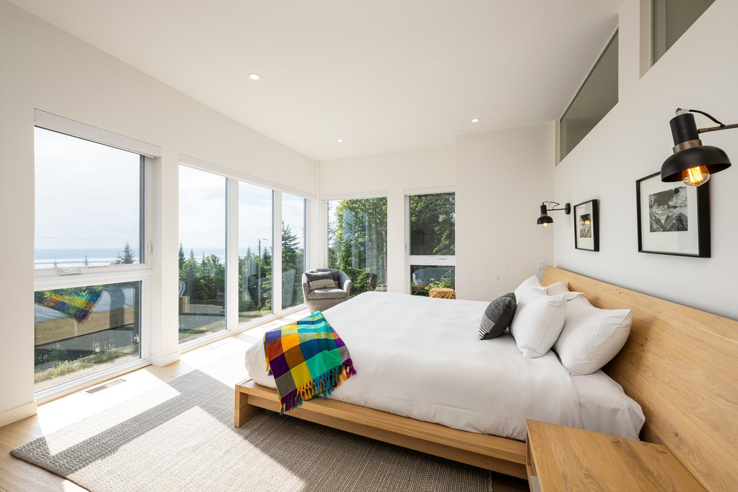 Chambre lumineuse avec un lit, grandes fenêtres et vue sur la mer.