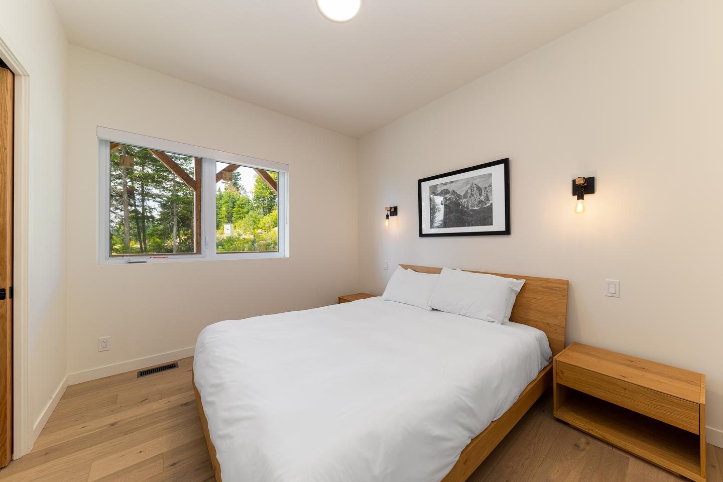 Chambre simple avec lit double, photo au mur, fenêtre et deux lampes murales.