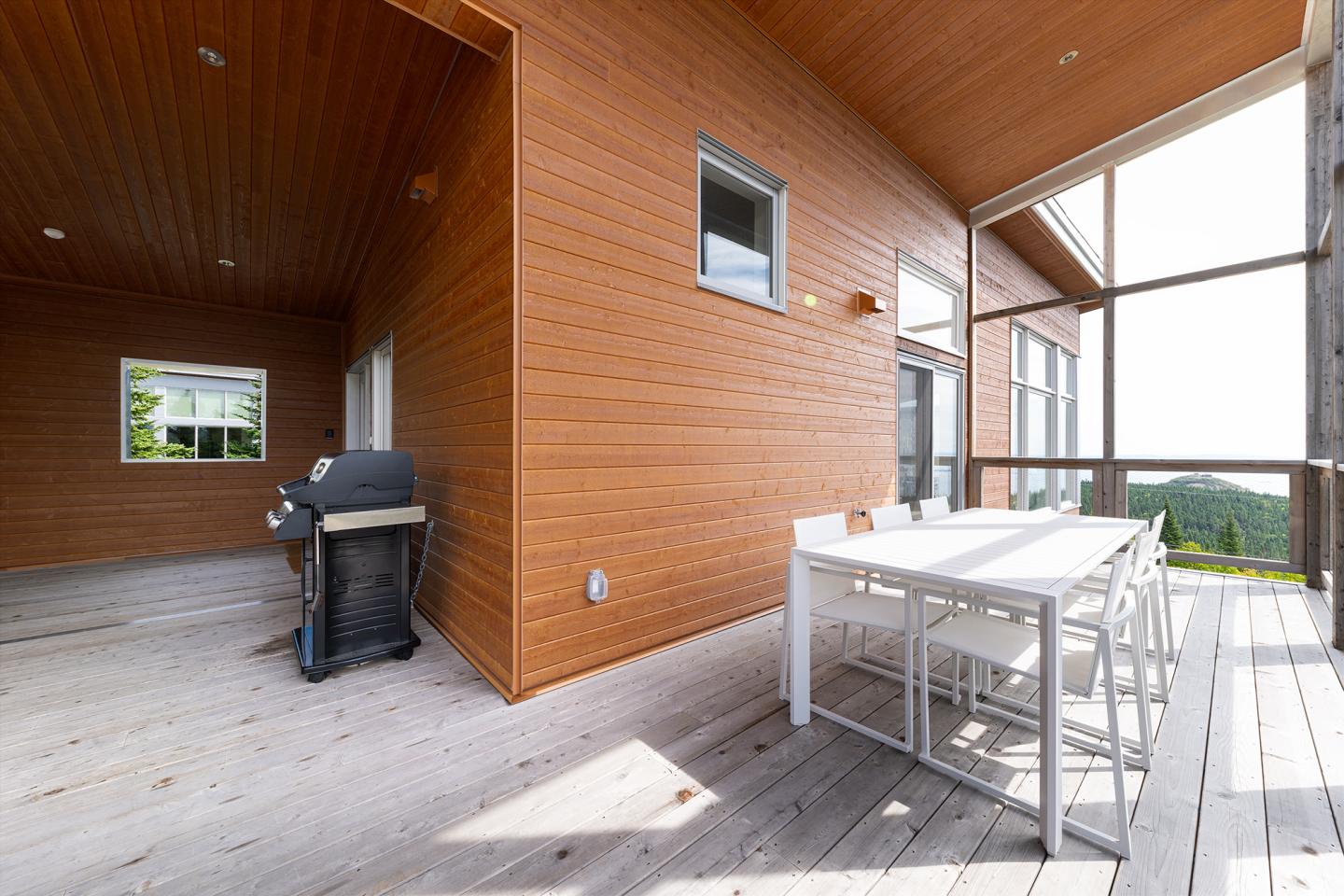 Terrasse en bois avec table blanche, chaises et barbecue.