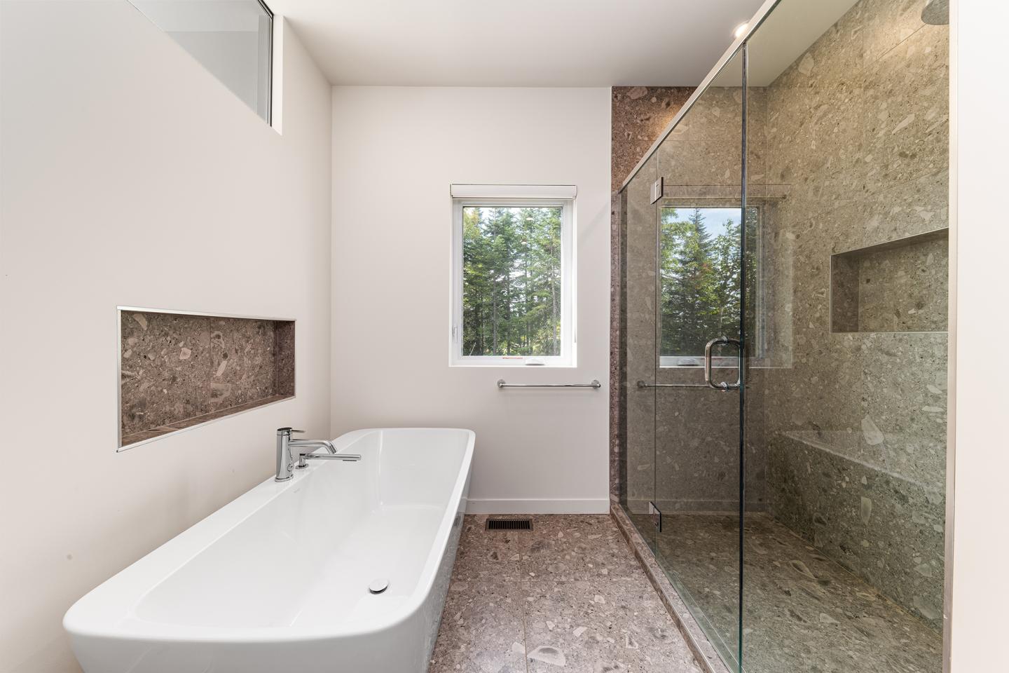 Salle de bain moderne avec baignoire blanche, douche vitrée et murs clairs.