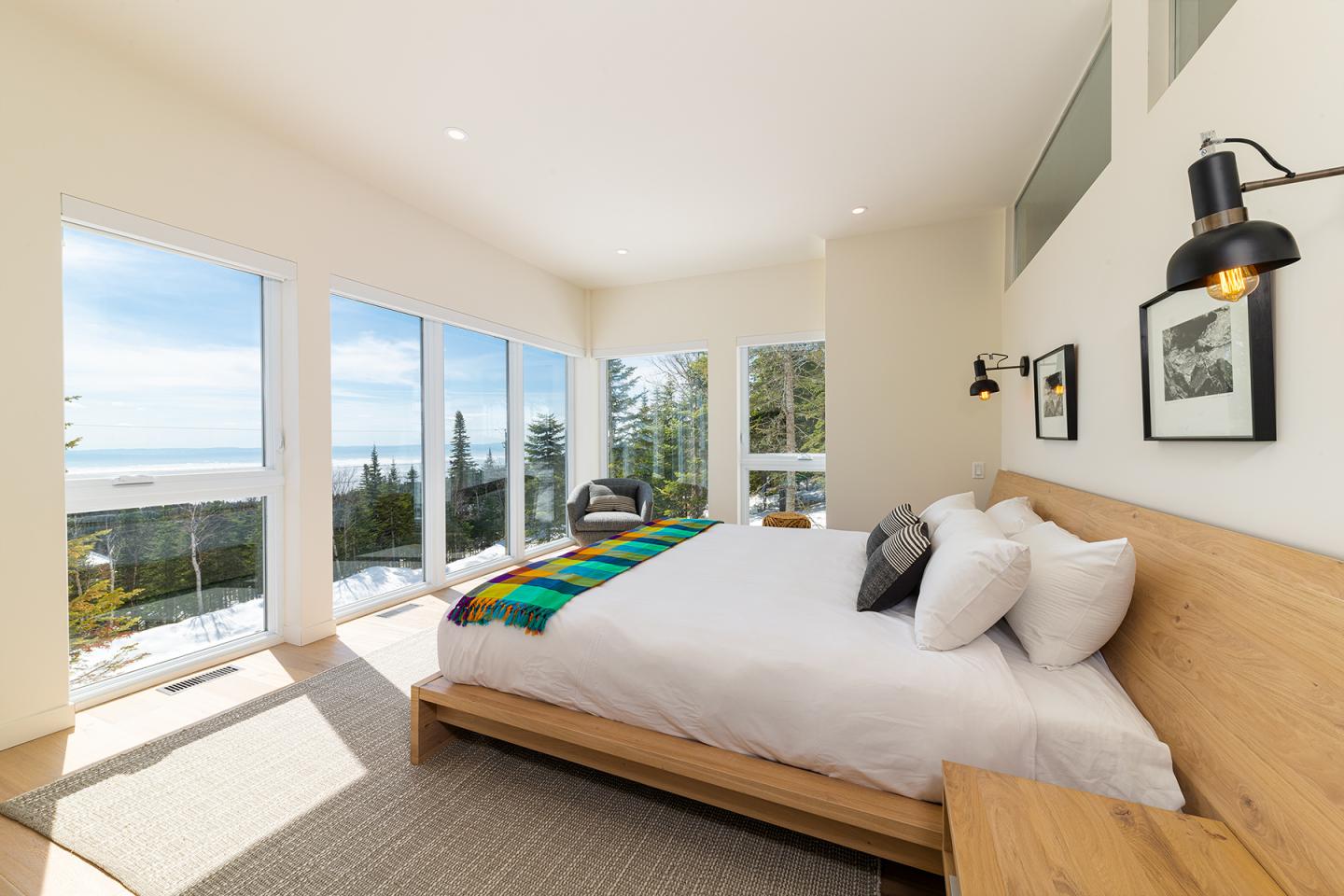 Chambre lumineuse avec grand lit blanc, baies vitrées et vue sur la mer.