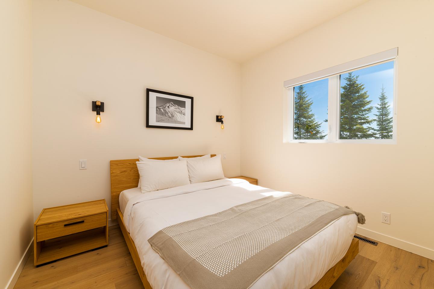Chambre lumineuse avec lit double, table de chevet, et fenêtre donnant sur des arbres.