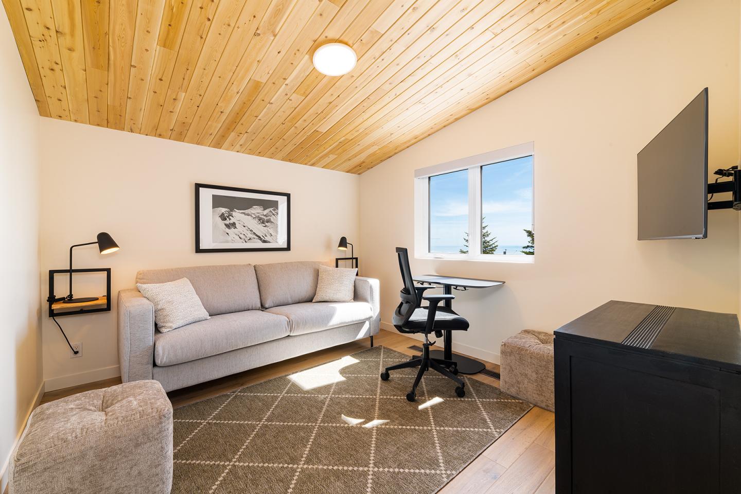 Salon avec canapé gris, bureau moderne et fenêtre avec vue dégagée.
